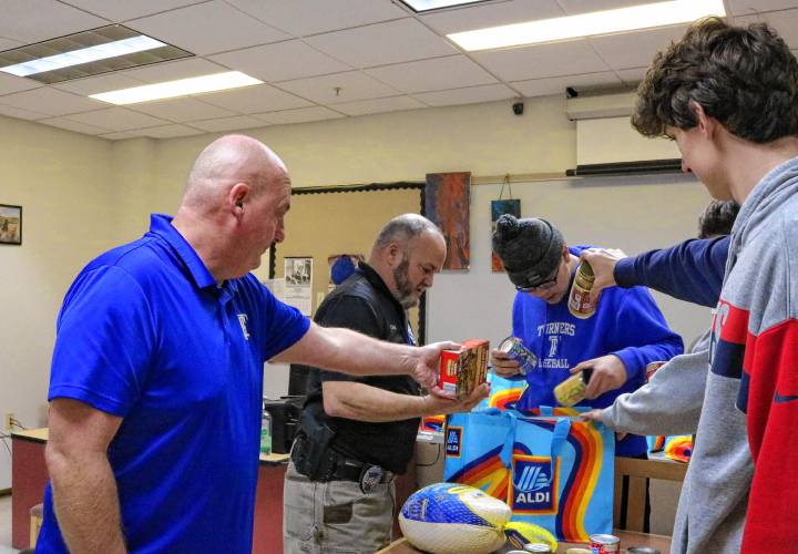 From left, Turners Falls High School Athletic Director Adam Graves and School Resource Officer Dan Miner work with students to pack food to be distributed to as many as 22 families ahead of Thanksgiving.