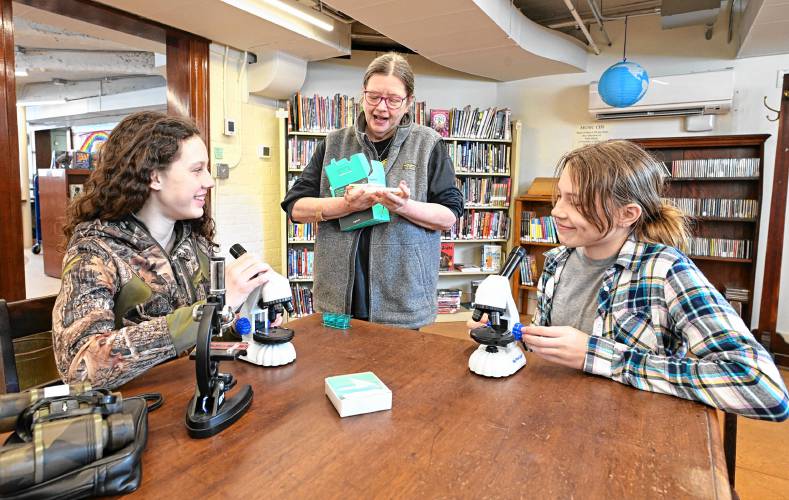 Library Director Laurie Wheeler, center, with Charlotte Smead of Heath and Juniper Totino of Charlemont, both 13, who are using microscopes at Arms Library in Shelburne Falls. The library is working to develop a “Library of Things” this spring.